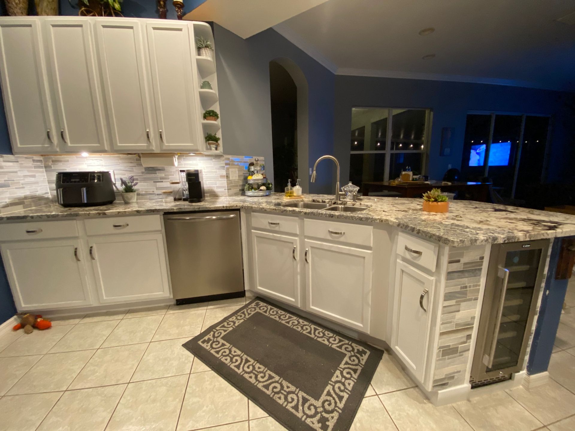 White kitchen cabinets with granite countertops, stainless steel appliances, and a gray rug on tiled floor.