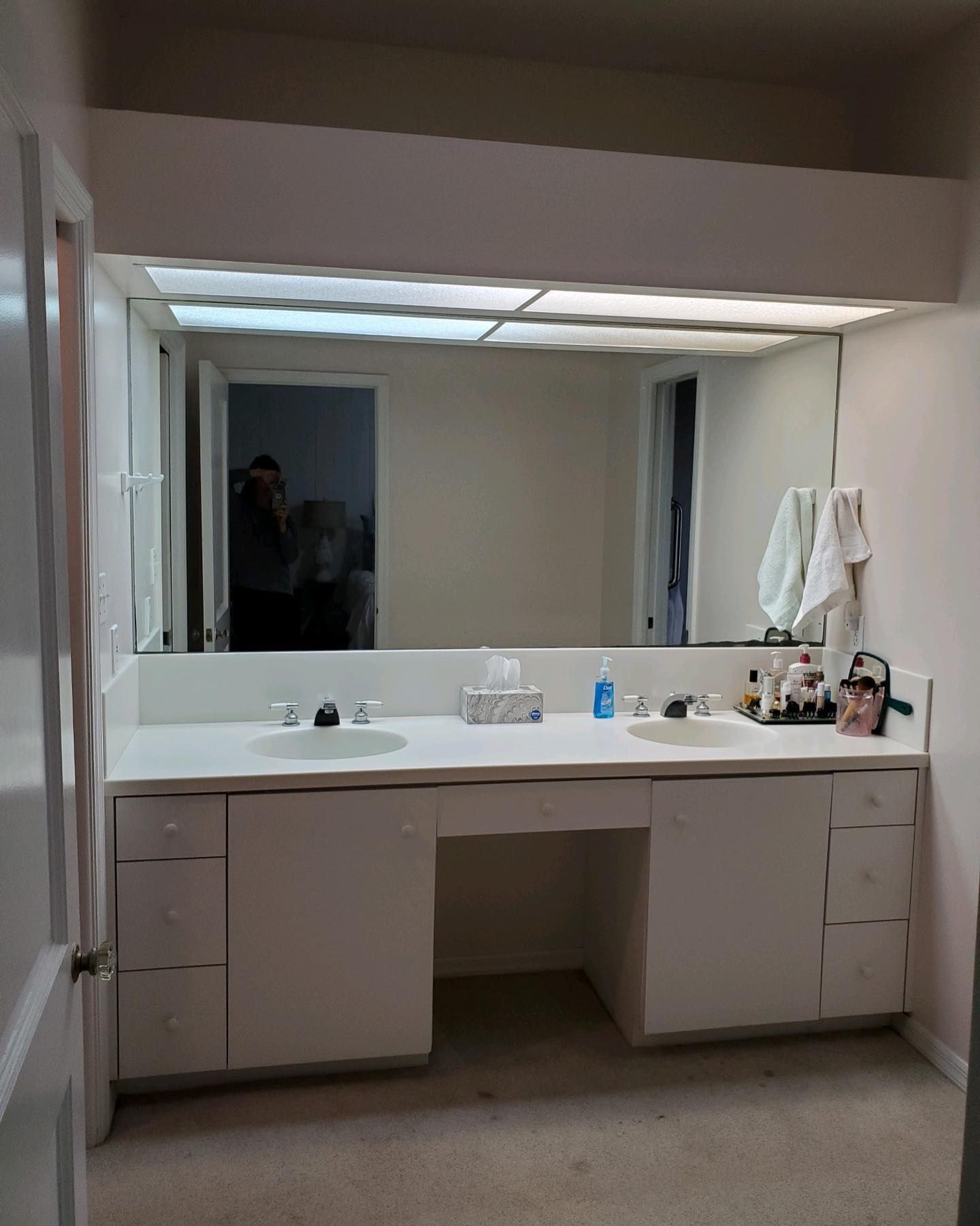 Bathroom vanity with large mirror, two sinks, and white cabinets.
