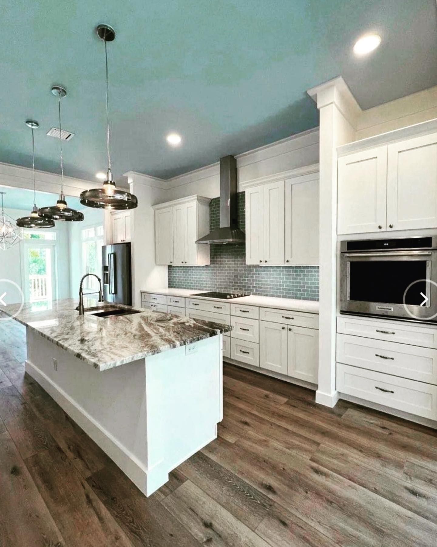 Modern kitchen with white cabinets, island, and granite countertops; hardwood floors.