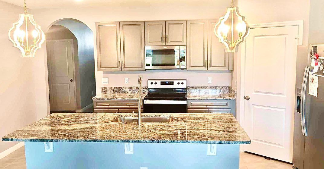 Kitchen with granite countertops, light cabinets, and blue island. Two decorative lights hang.