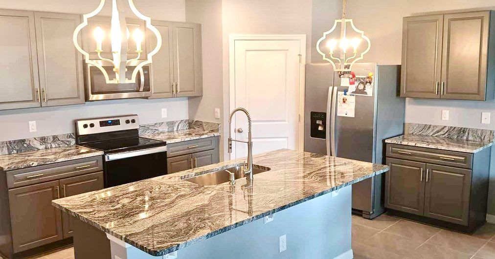 Modern kitchen with gray cabinets, granite countertops, island, stainless steel appliances, and decorative lighting.