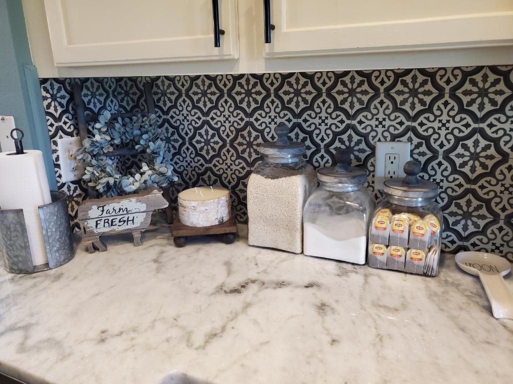 Kitchen counter with jars of ingredients and decorative items against patterned tile backsplash.