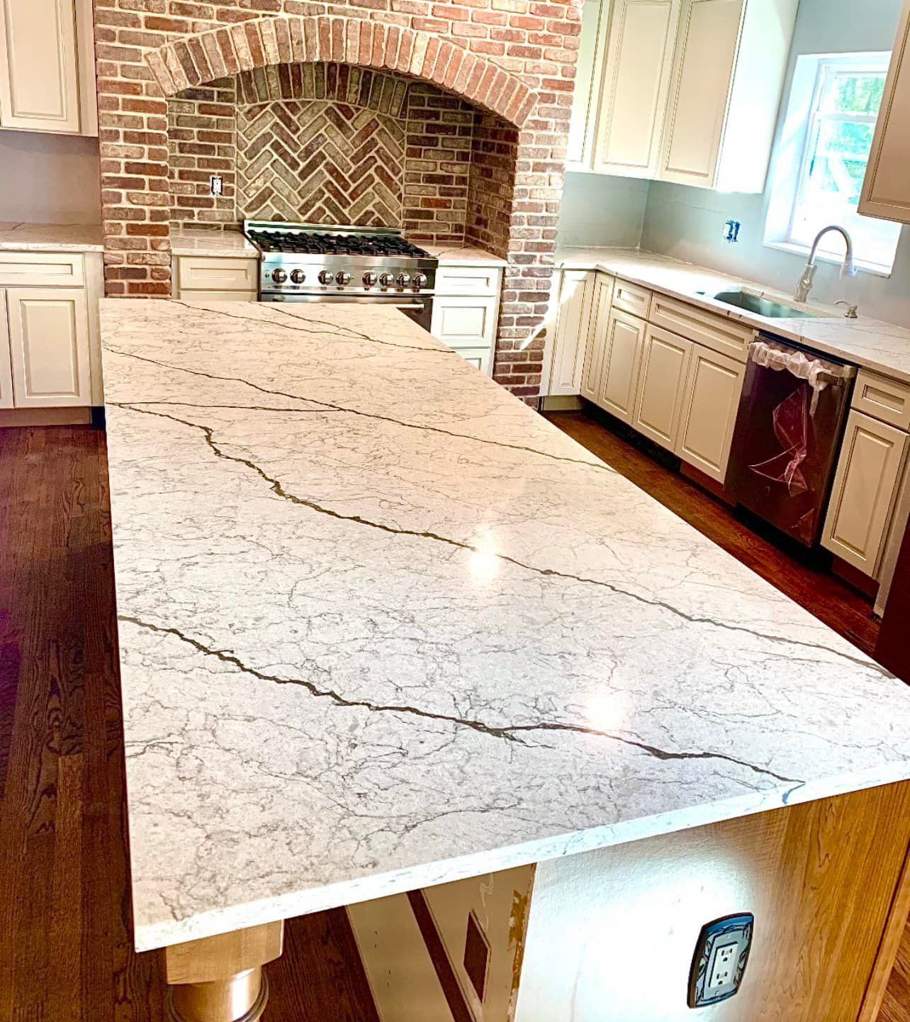 Kitchen with large island, marble countertop, brick stove alcove, cream cabinets, and wood flooring.