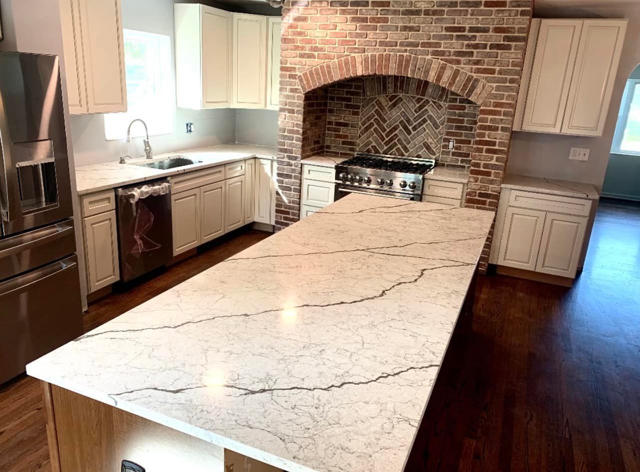 Kitchen with large island, brick arch, off-white cabinets, stainless steel appliances, and dark wood floors.