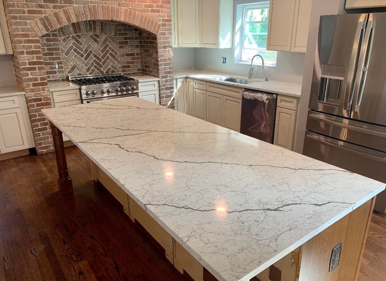 A kitchen with a large island countertop, brick backsplash, stainless steel appliances, and cream cabinets.