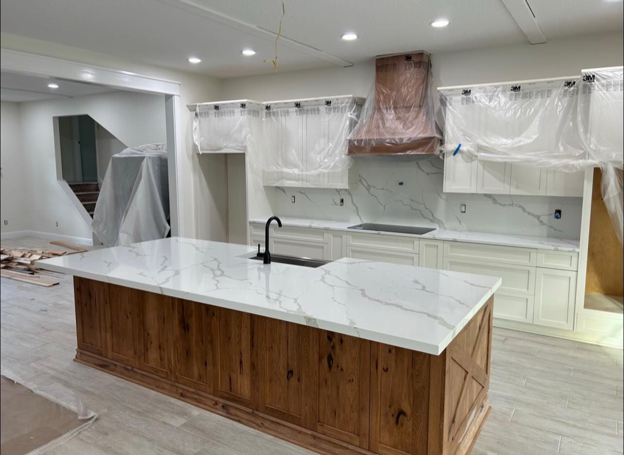 Kitchen renovation with white marble countertops, wooden island, and white cabinets under construction.
