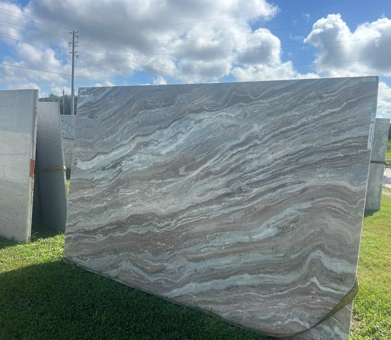 Large slab of brown, beige and white marble outdoors, wavy pattern.