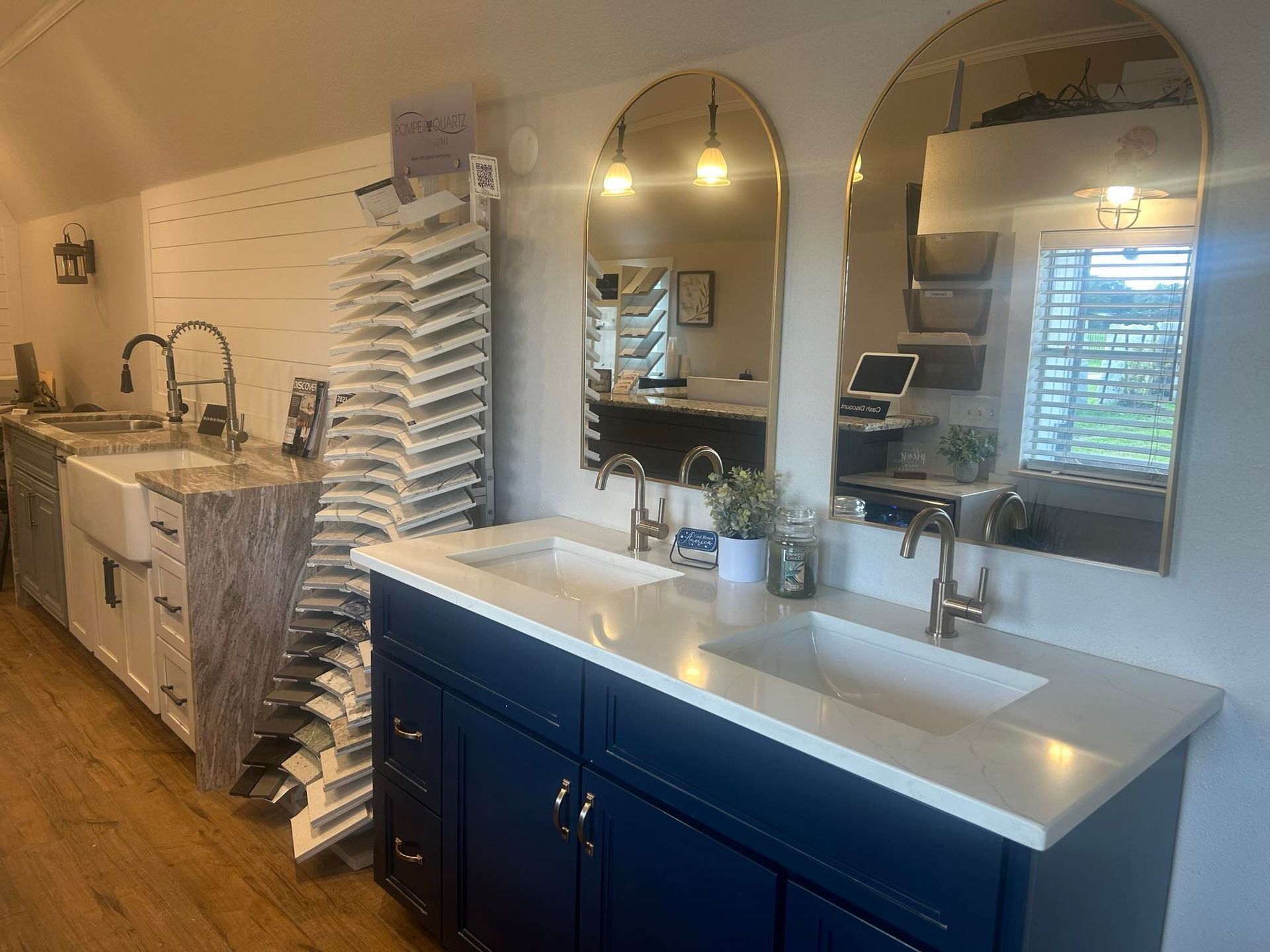 Bathroom showroom: blue double vanity, arched gold mirrors, sink displays, and white shiplap walls.