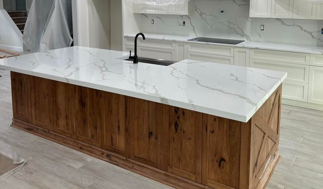 Kitchen island with white marble countertop and wood paneling. Black faucet.