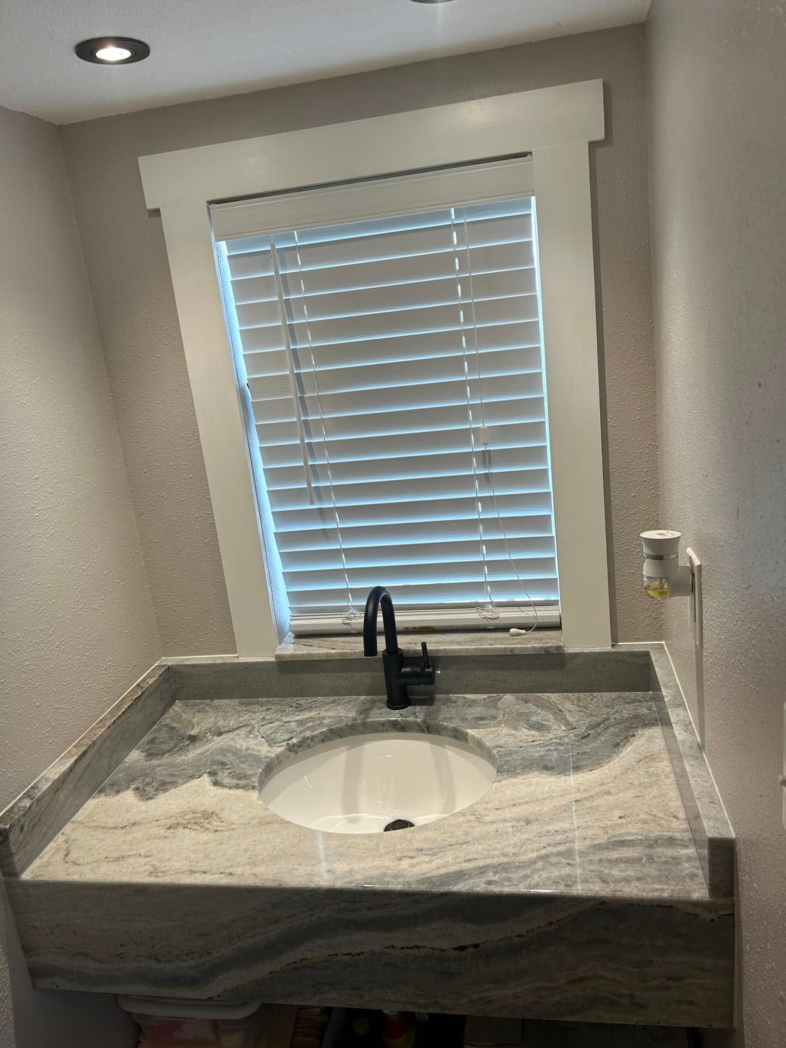 Bathroom vanity with a granite countertop, black faucet, and window with blinds.