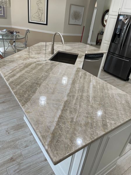Kitchen island with light brown marble countertop, sink, faucet, and dishwasher. White cabinets.