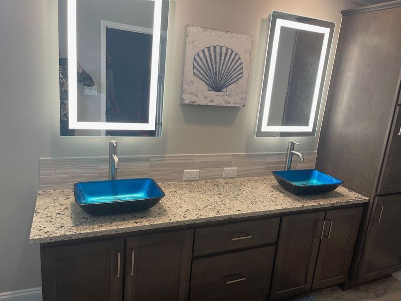 Bathroom vanity with two blue glass sinks, lighted mirrors, and brown cabinets.