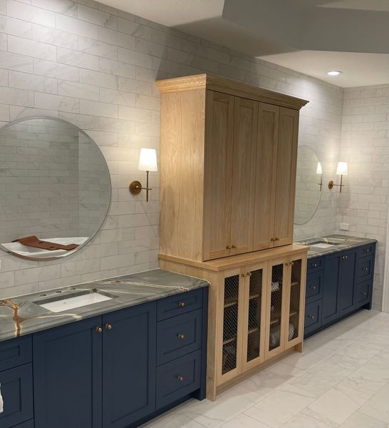 Bathroom with blue vanities, round mirrors, and a light wood cabinet between them.