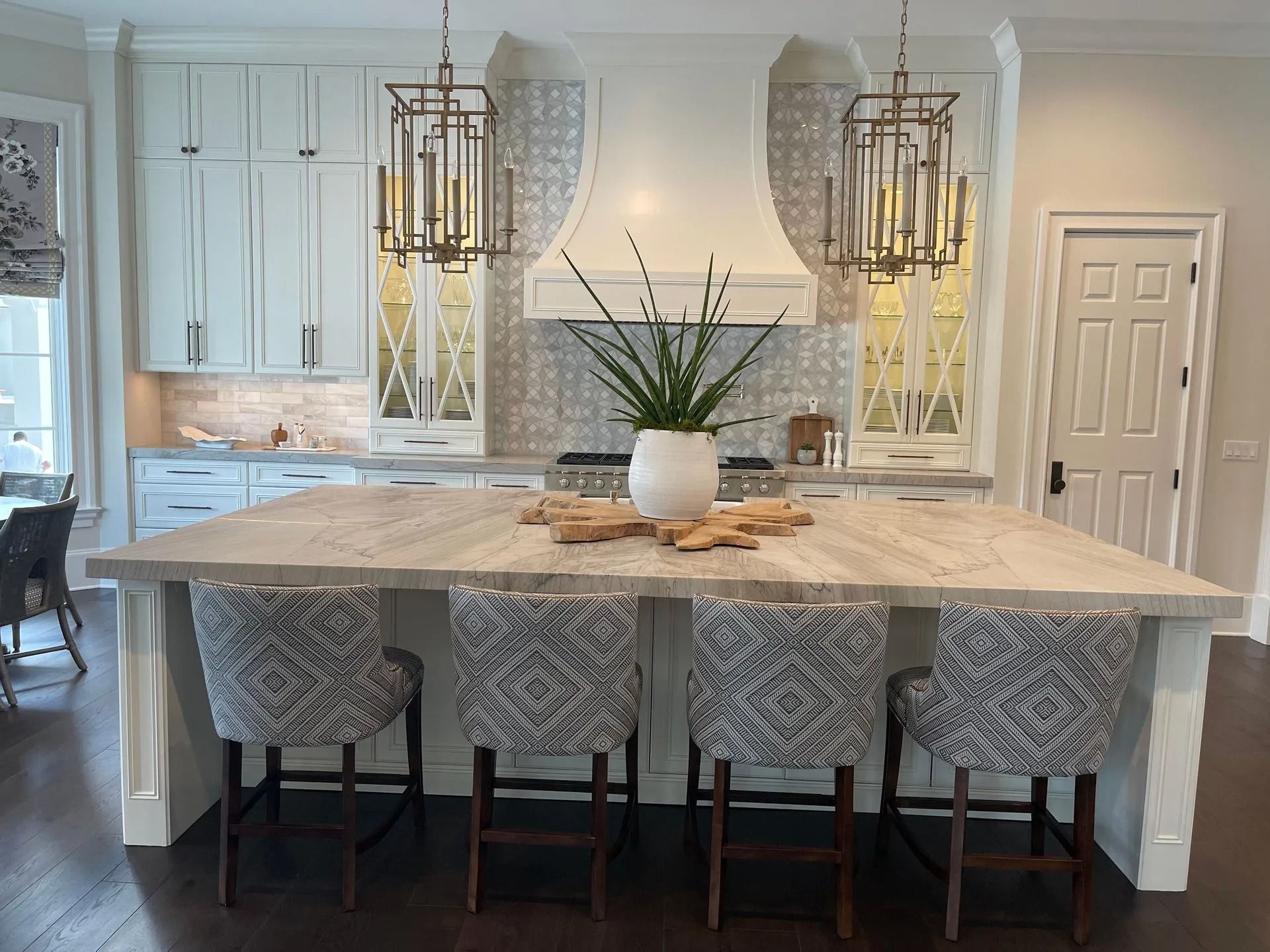 Elegant kitchen with large island, four patterned bar stools, white cabinetry, range hood, and pendant lights.