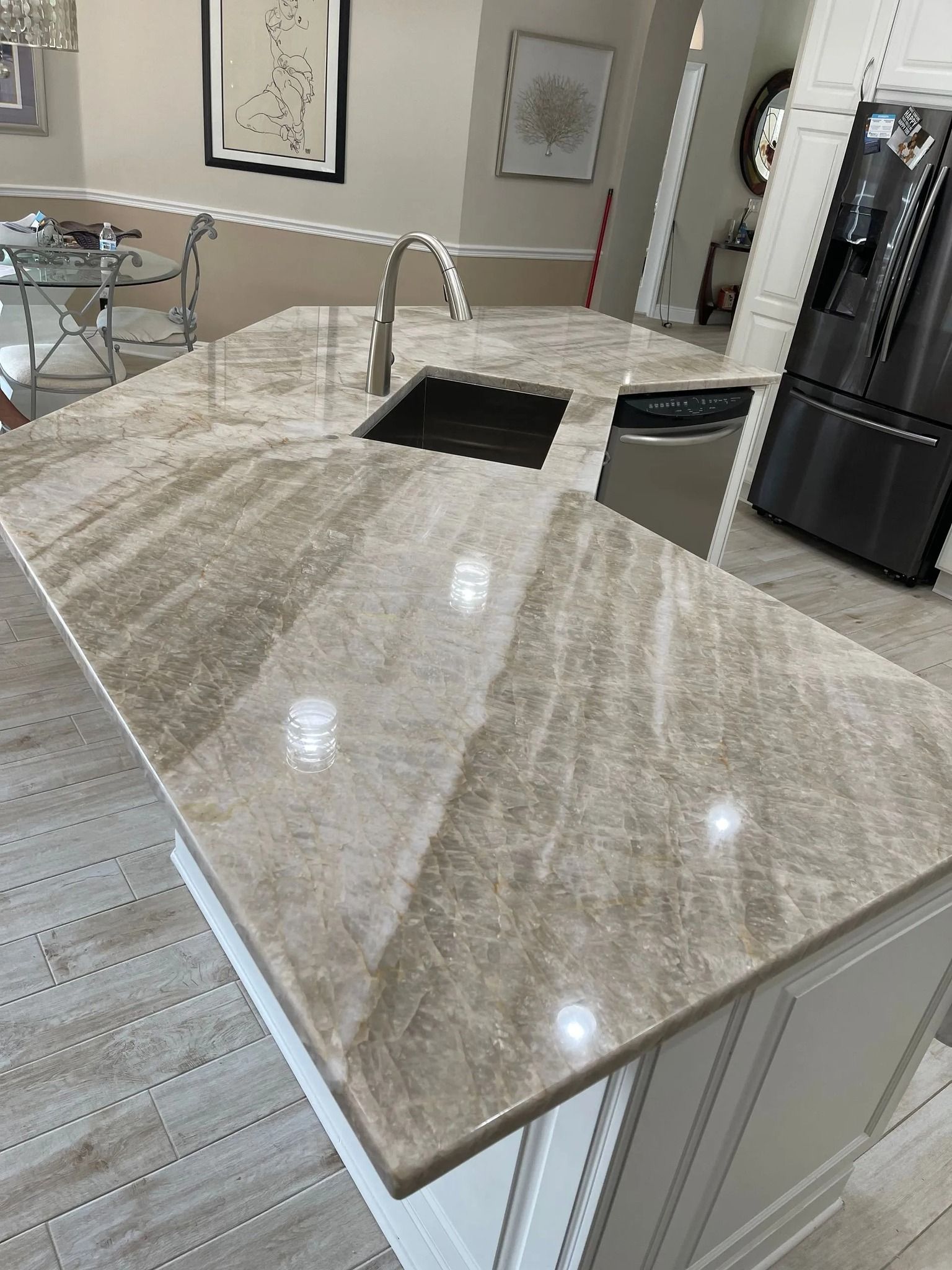 Kitchen island with a marble countertop, sink, faucet, and dishwasher. White cabinets, stainless steel appliances.