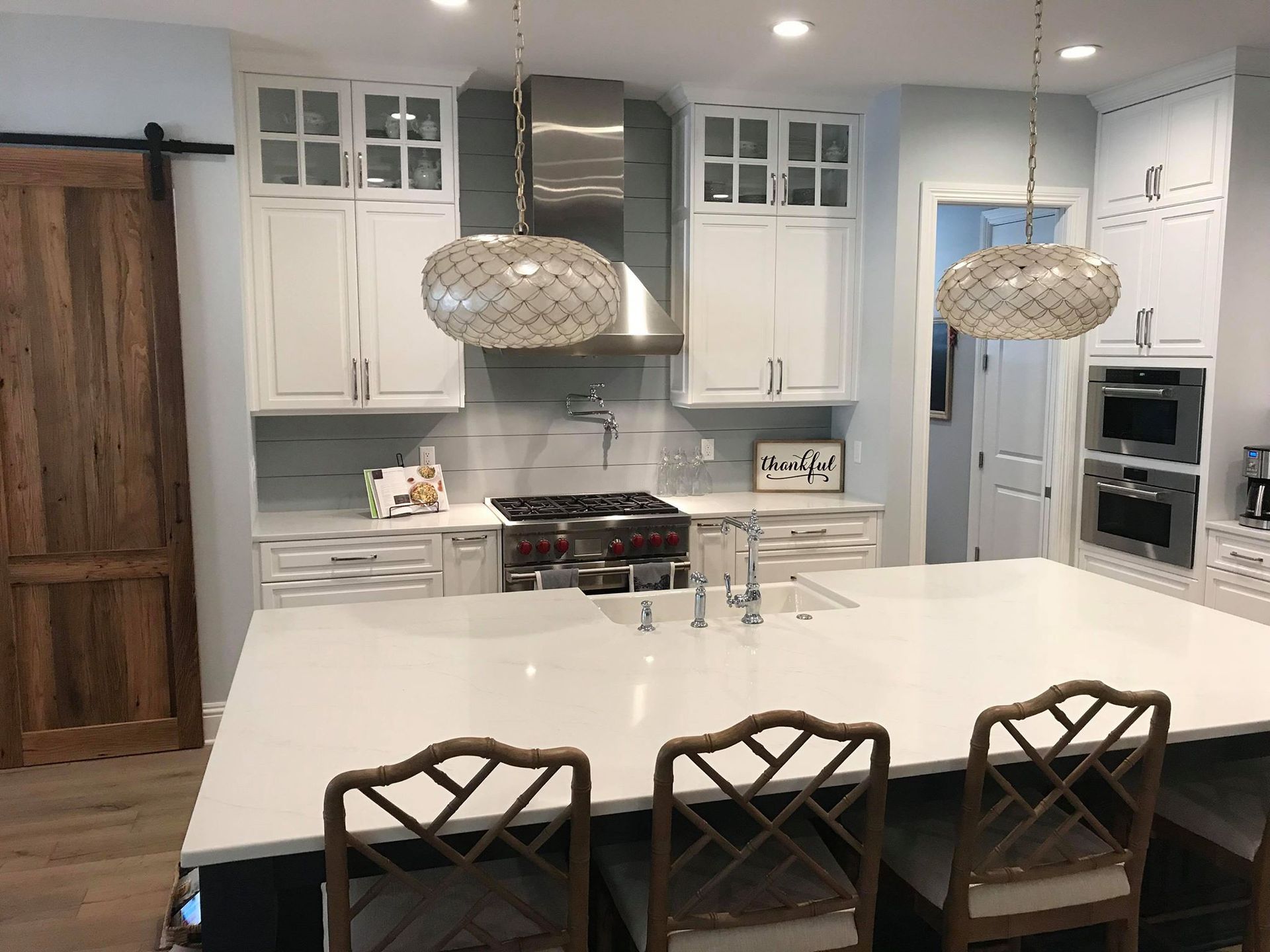 Bright white kitchen with large island, stainless steel appliances, and two decorative pendant lights.