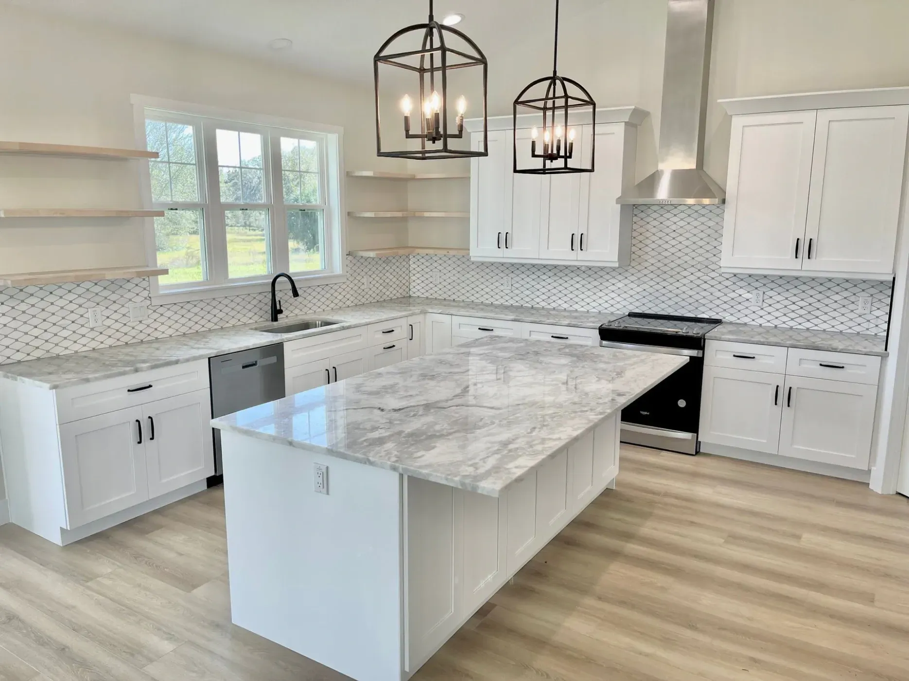 Modern white kitchen with island, marble countertops, and black light fixtures.