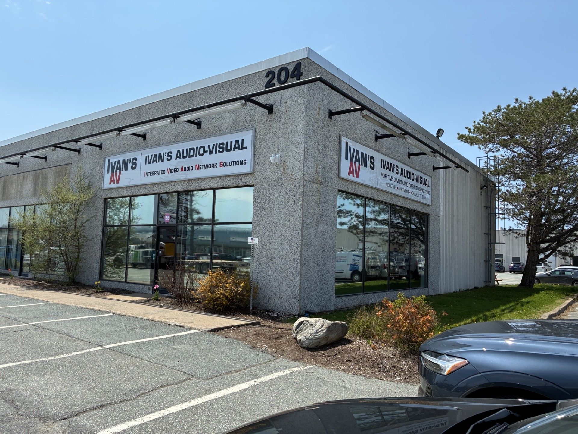 Exterior of a glass-fronted business office with a sign, parking lot, and a car in front