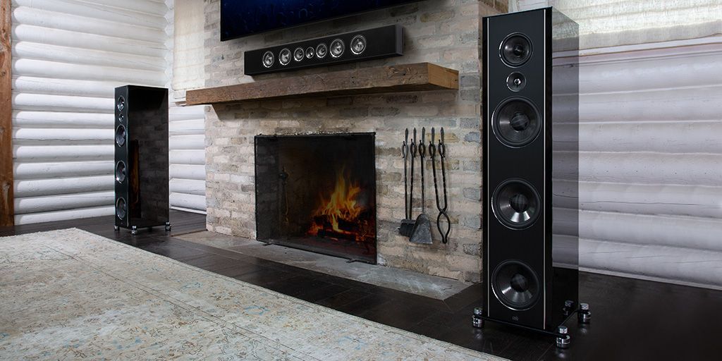 Modern living room fireplace with tall black speakers on either side and a lit fire inside the brick hearth