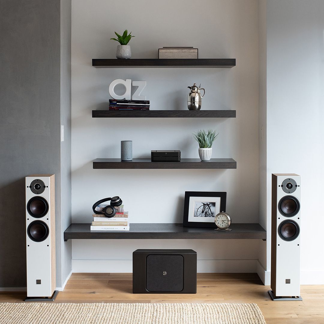 Modern living room with floating shelves, speakers, and a TV stand on a light wood floor.