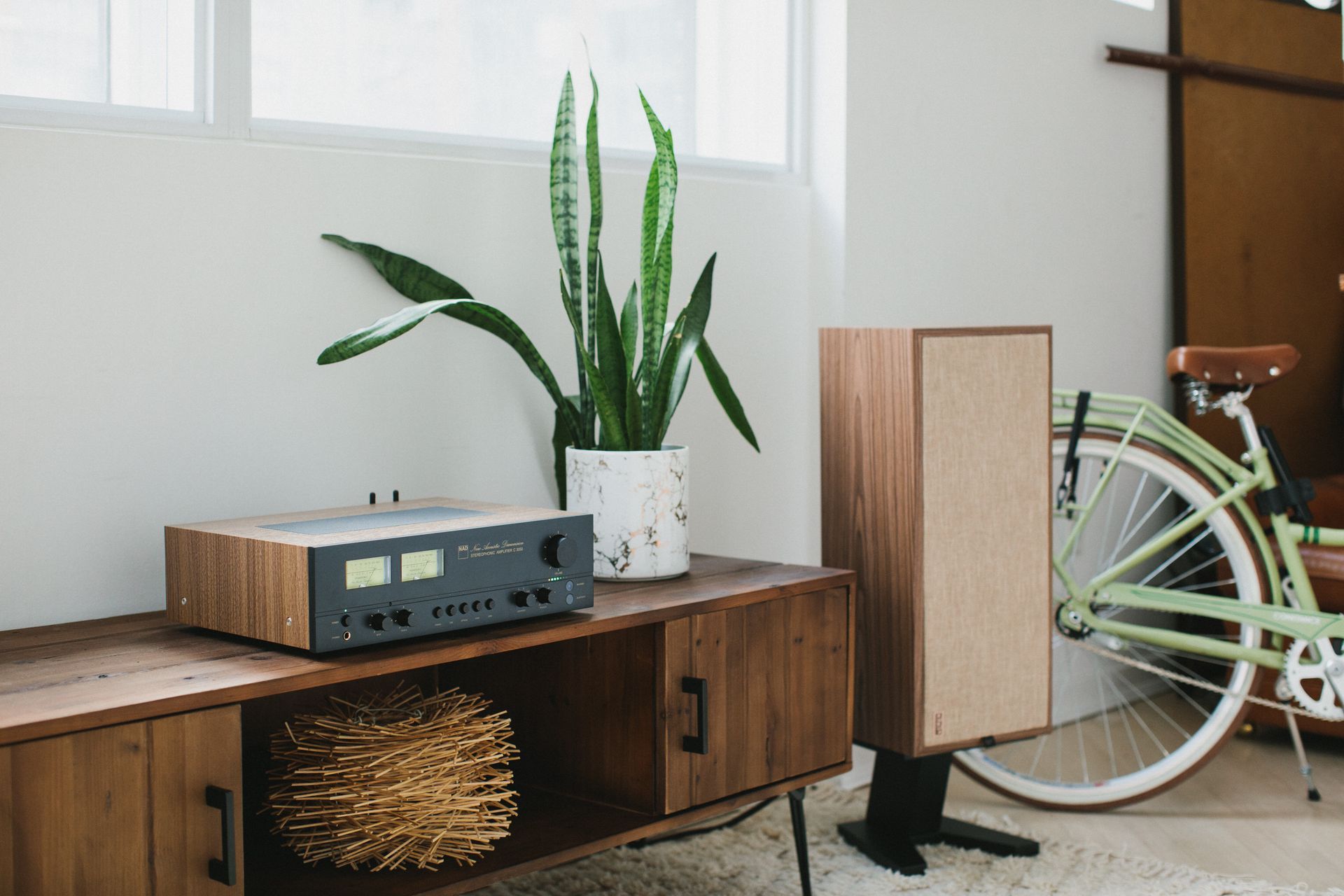 Modern living room with a wood console, speaker, potted plant, and a bicycle near a window