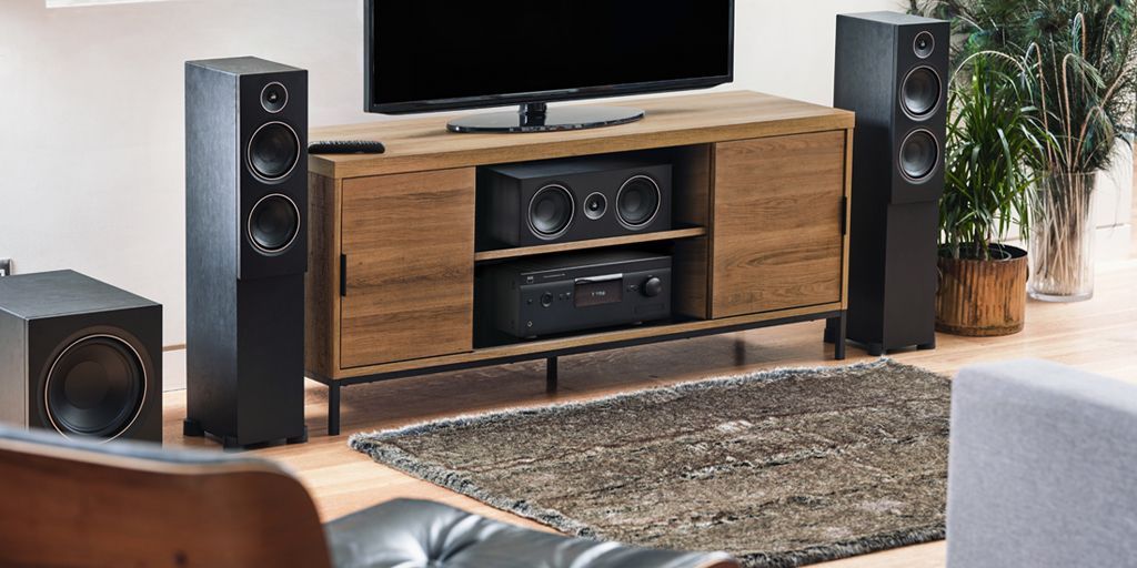 Modern living room with TV, wood media console, tall speakers, subwoofer, and rug