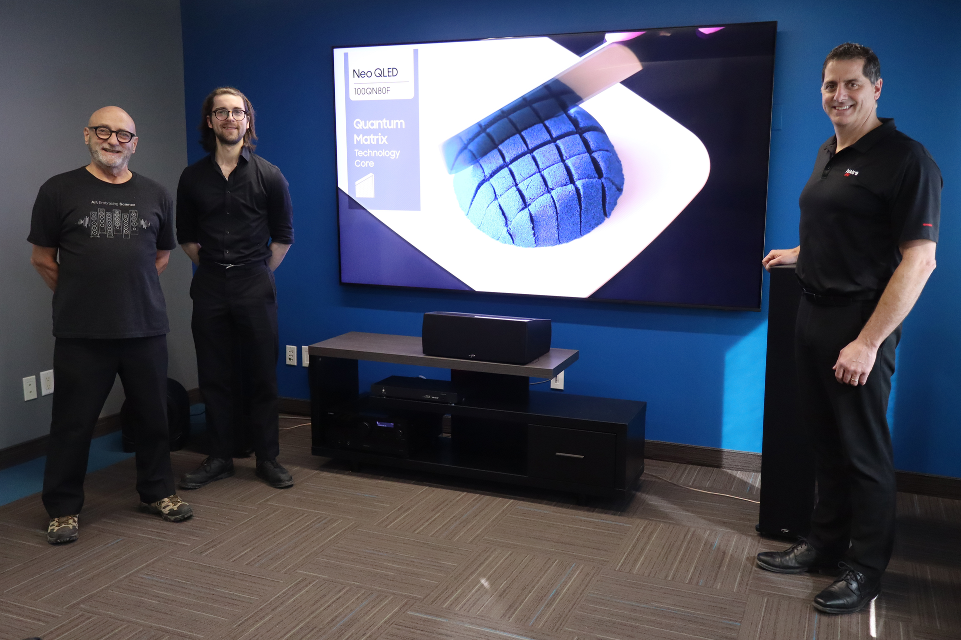 Three people stand beside a large display showing a blue 3D grid model in a demo room.