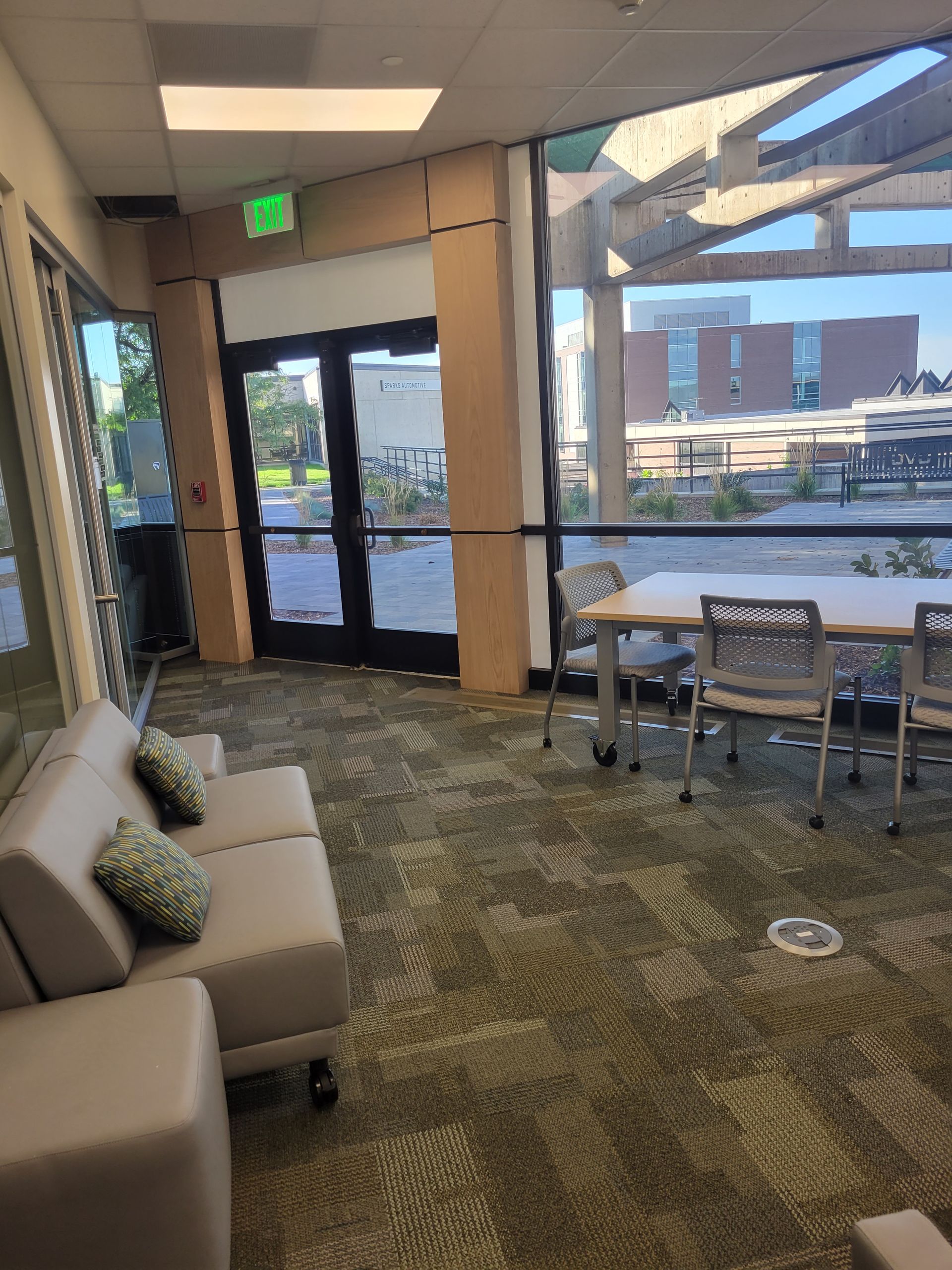 Waiting area with beige sofa, chairs, large windows, and glass entrance doors in a modern lobby