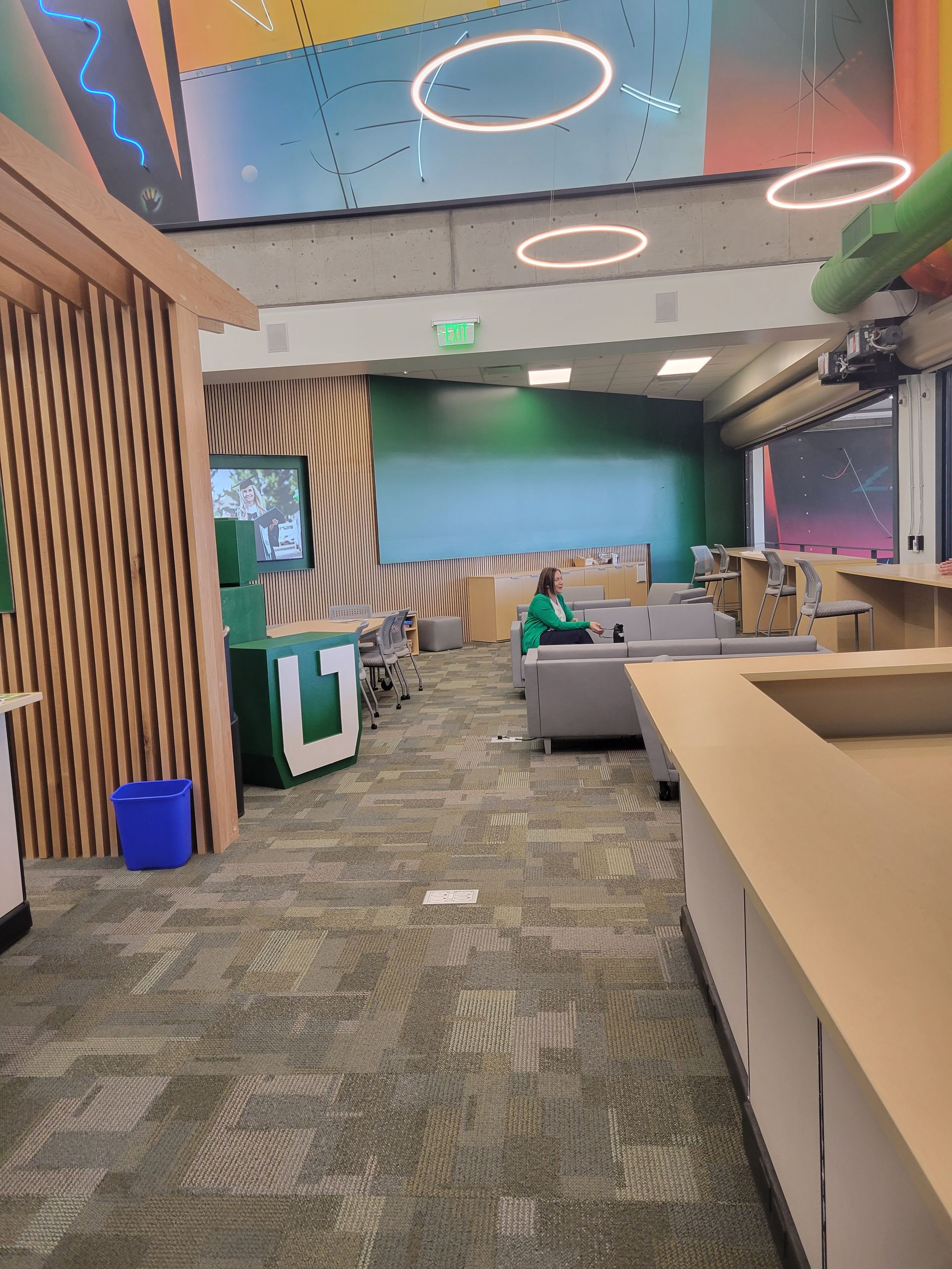 Modern office lounge with patterned carpet, wood slats, green accents, and empty seating areas