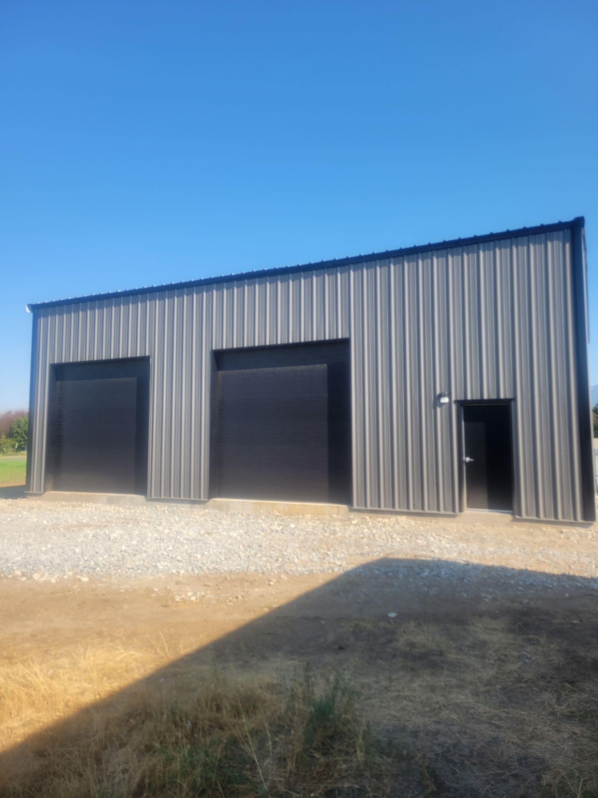Gray metal warehouse with three garage doors on a gravel lot under a blue sky