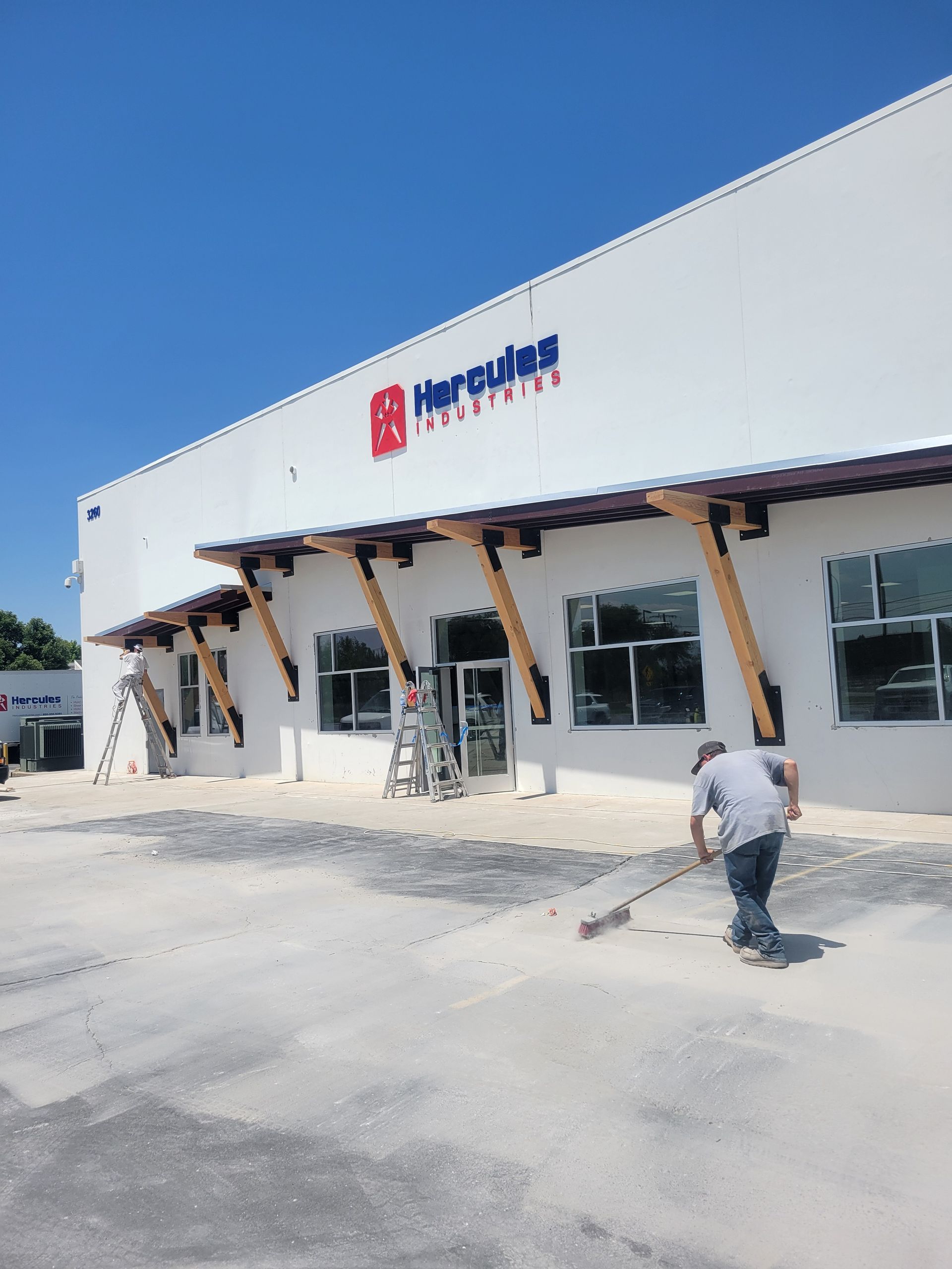 Large white warehouse with red awnings and a person walking on a paved lot under a blue sky