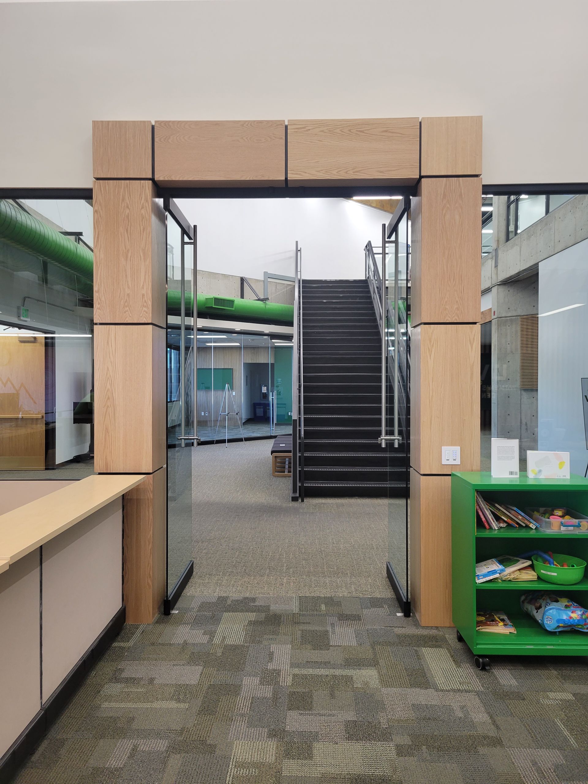 Indoor corridor with wooden archway, stairs ahead, and green storage shelf on the right.