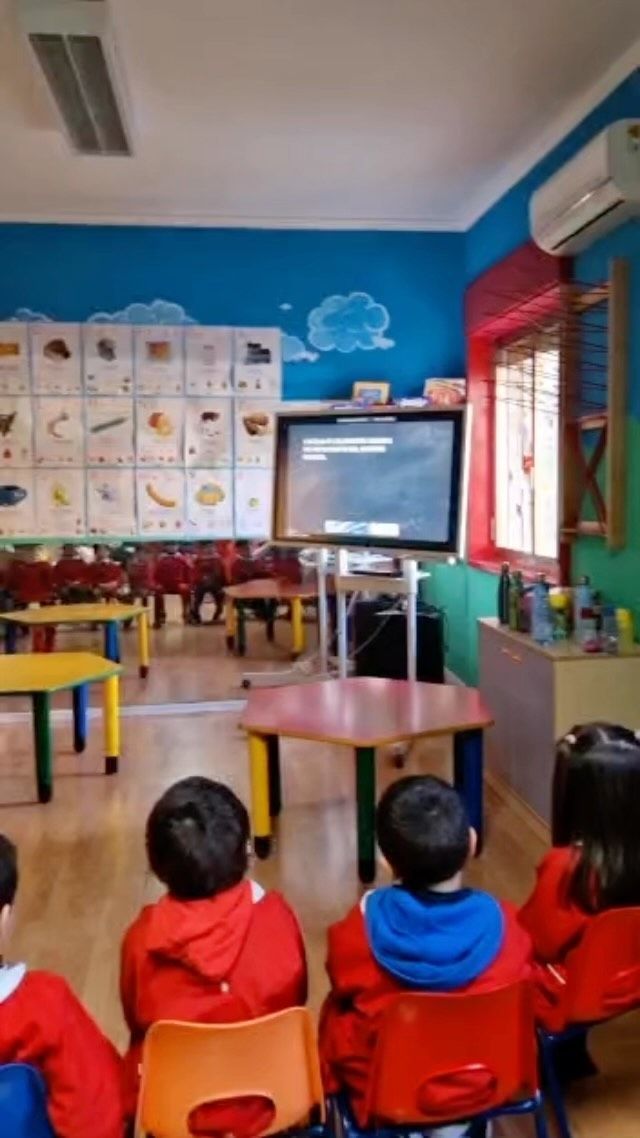 Bambini seduti davanti alla TV in un'aula colorata.