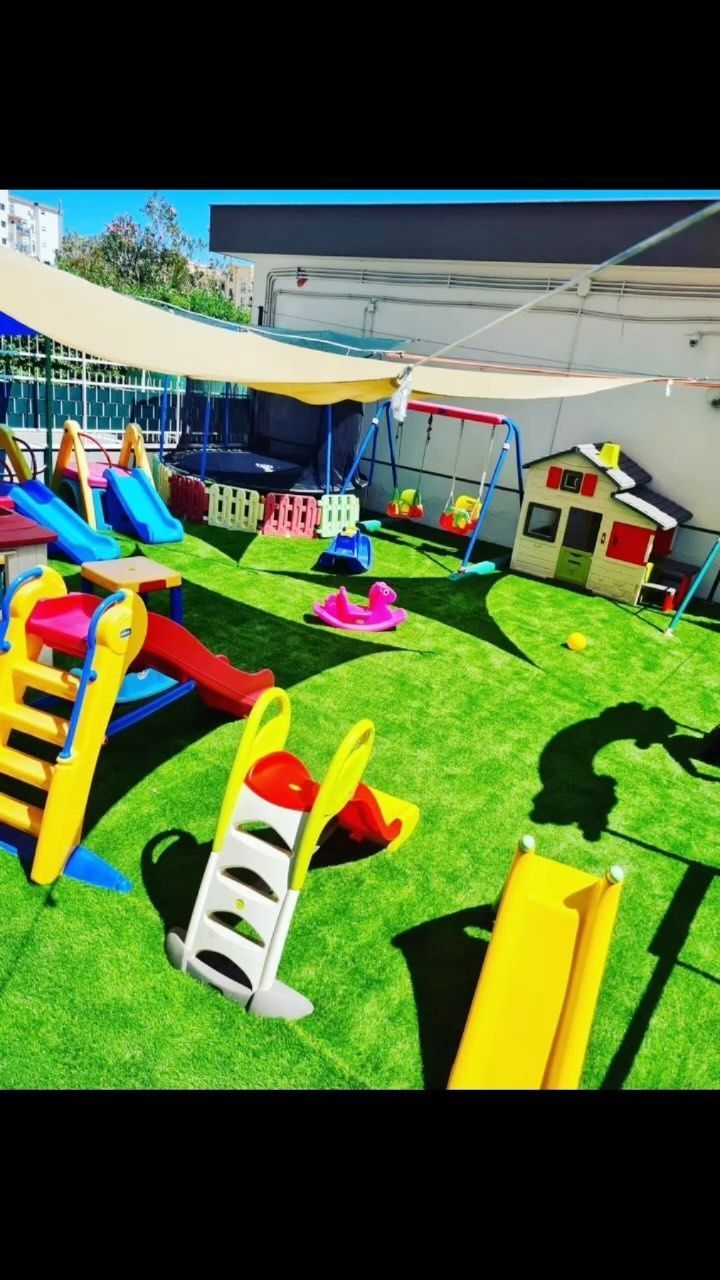 Parco giochi con scivoli colorati, altalene e casetta da gioco su prato verde.