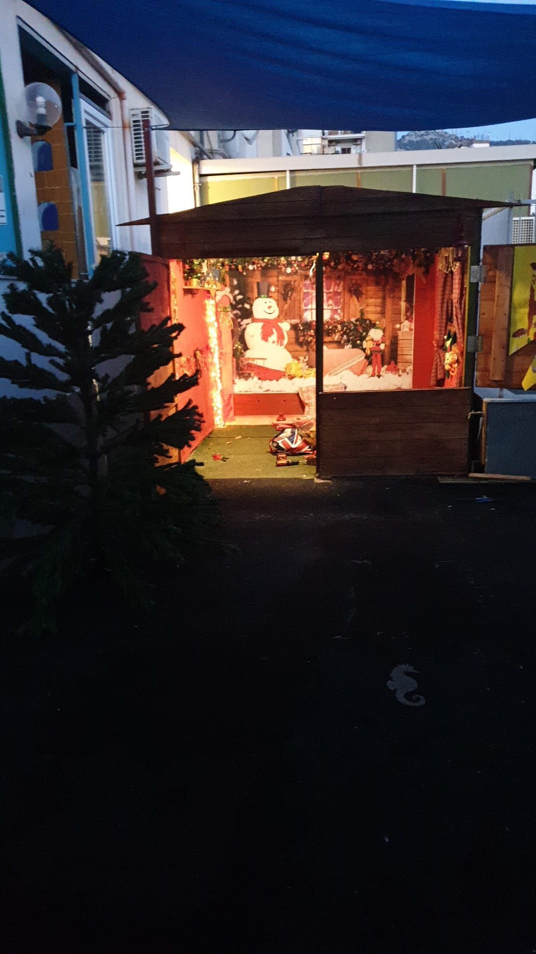 Vetrina illuminata a festa sotto una tenda blu al crepuscolo, con una piccola decorazione luminosa all'interno.
