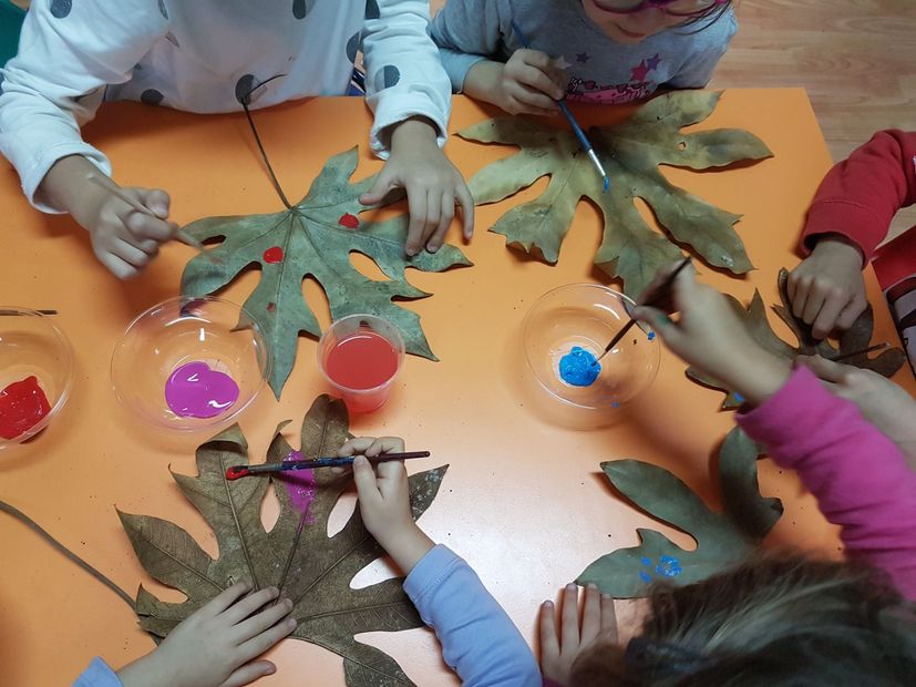 Bambini che dipingono grandi foglie con diversi colori seduti a un tavolo.