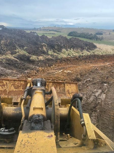 A Bulldozer Is Moving Dirt In A Field With Mountains — About Time Plumbing & Civil Construction in Bowral, NSW