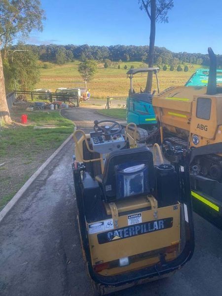 A Caterpillar Roller Is Driving Down A Dirt Road — About Time Plumbing & Civil Construction in Goulburn, NSW