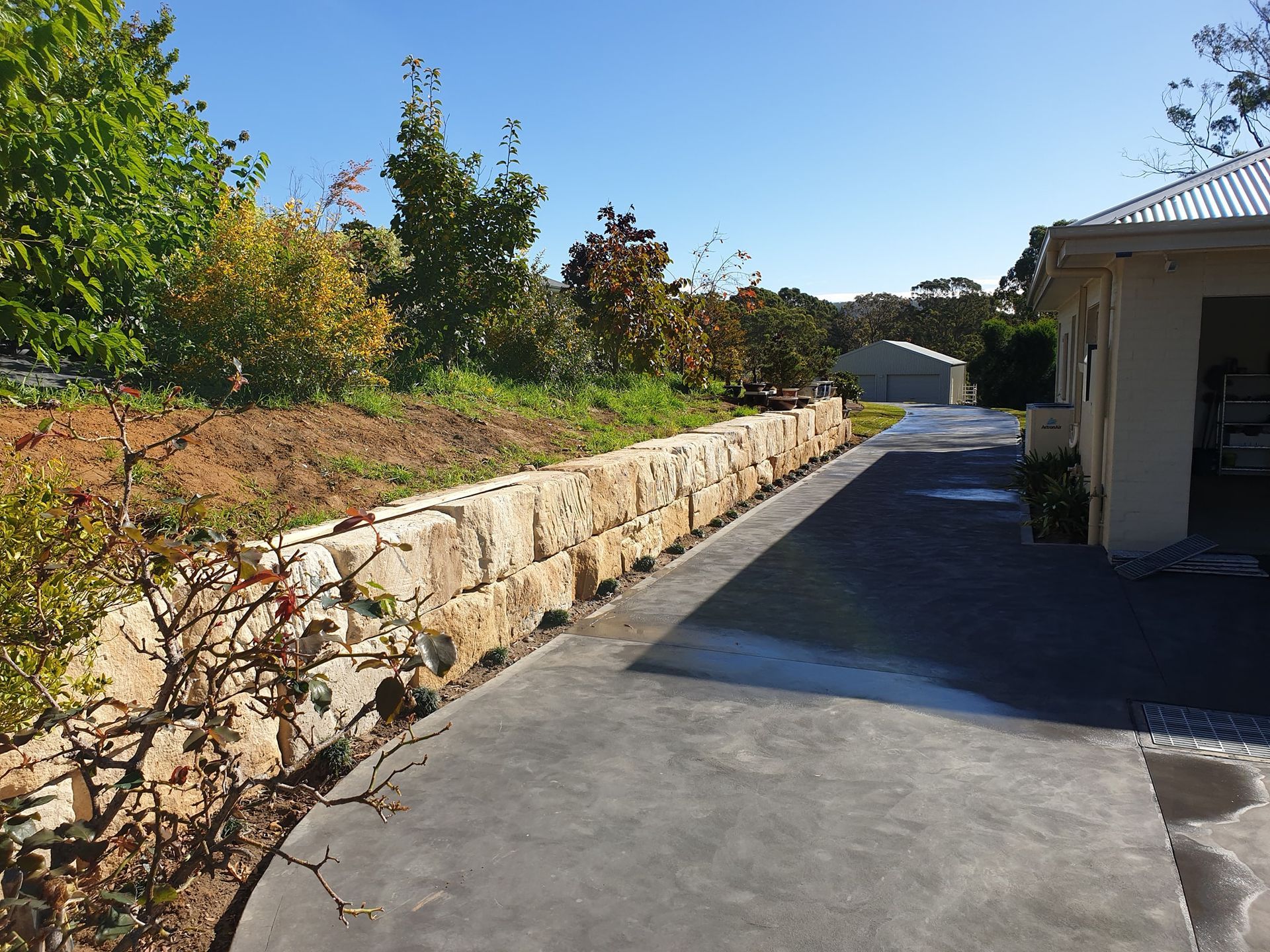 A Driveway Leading To A House With A Stone Wall — About Time Plumbing & Civil Construction in Moss Vale, NSW