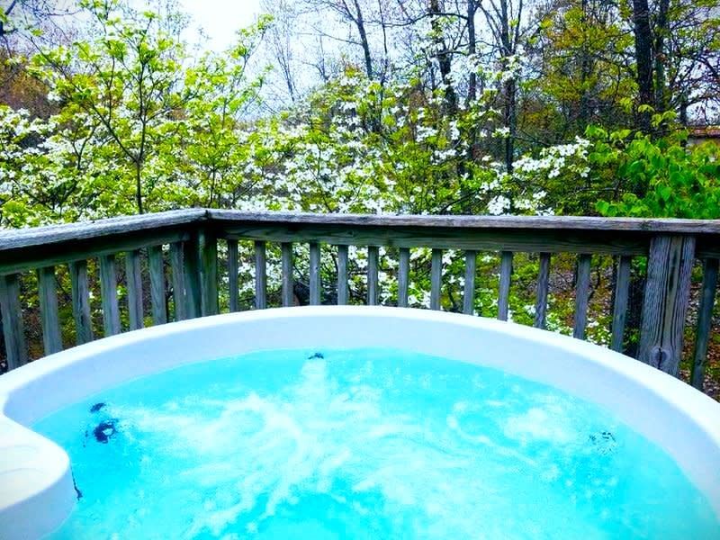 A hot tub is on a deck with trees in the background.