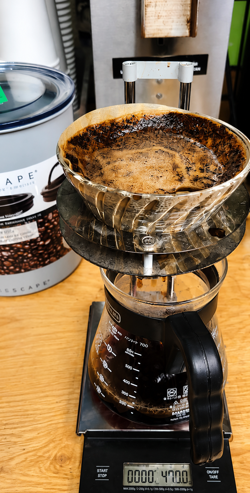 Pour-over coffee brewing in a glass dripper over a digital scale on a wooden counter.