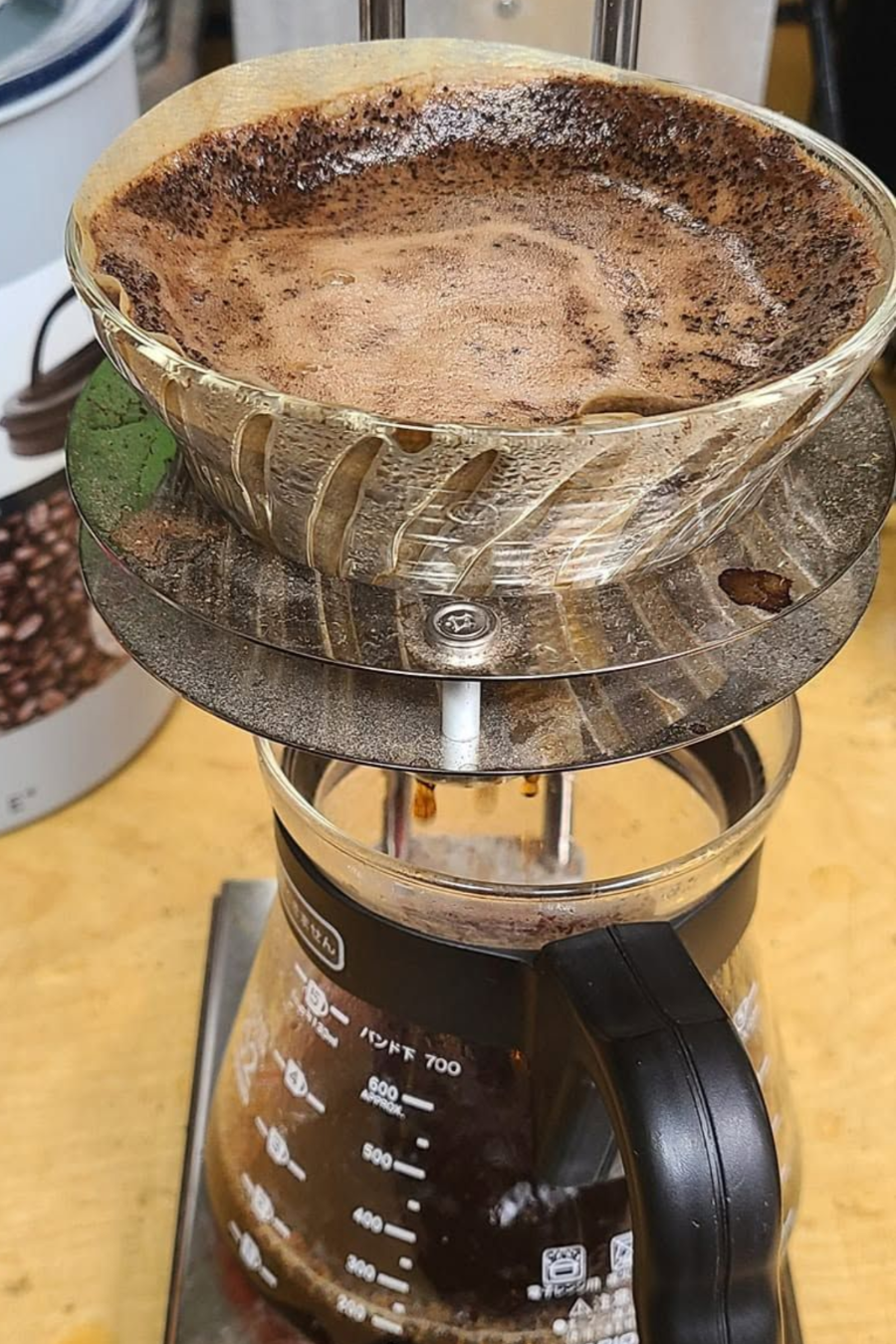 Coffee grounds in a grinder bowl above a glass coffee carafe on a kitchen counter.