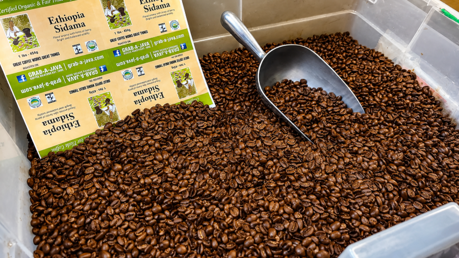 Scoop in a bin of roasted coffee beans with small product labels in the corner