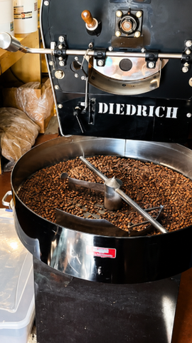 Coffee beans in a roaster drum labeled Diedrich, with beans tumbling inside.