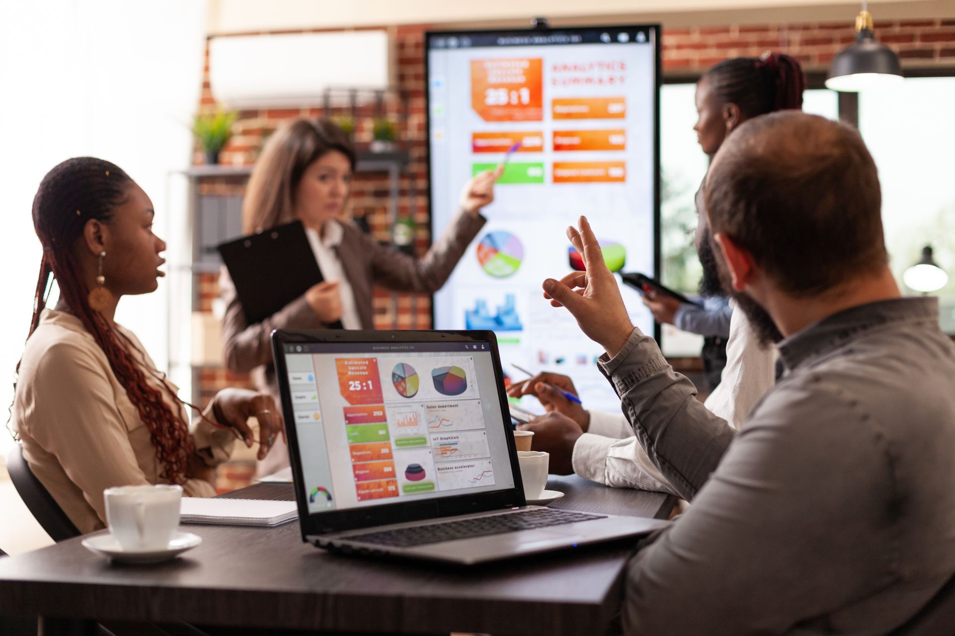 Team meeting in a conference room with laptops and a presenter showing charts on a screen