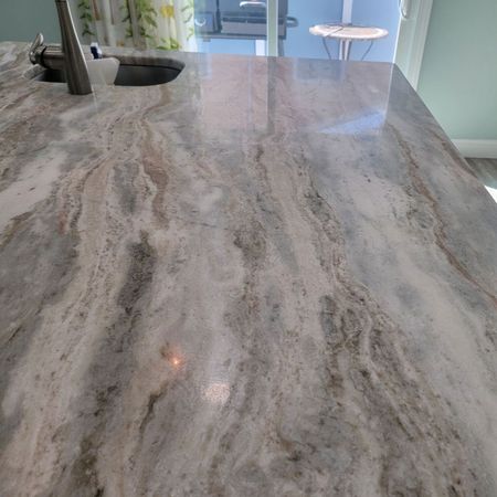 Close-up of a kitchen countertop with flowing gray, brown, and white marble-like patterns, reflecting light.