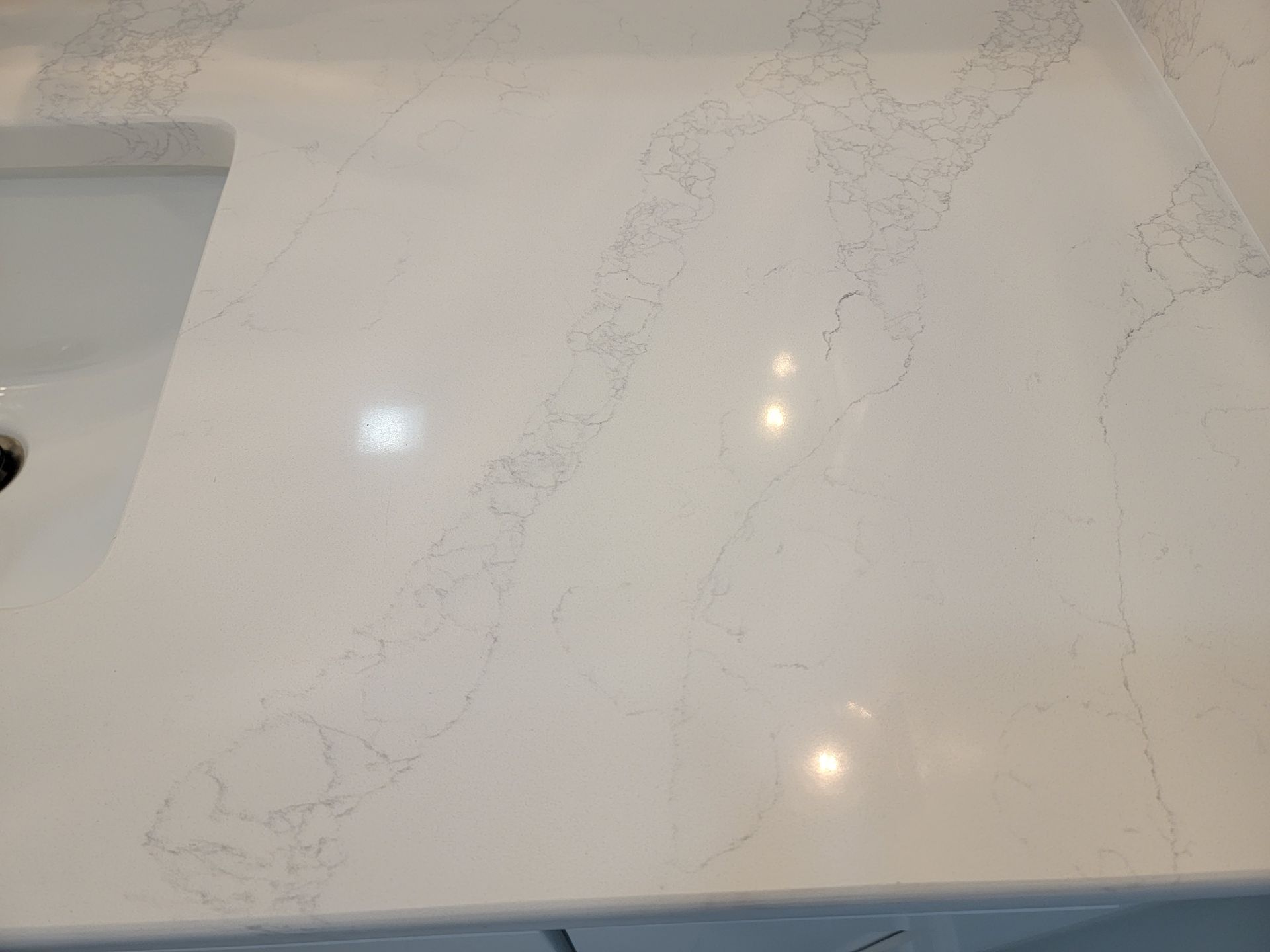 White countertop with gray veining near a sink basin.
