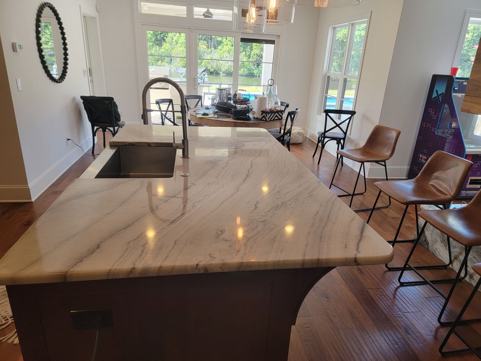 Kitchen with marble countertop, island, sink, bar stools, and view of backyard.