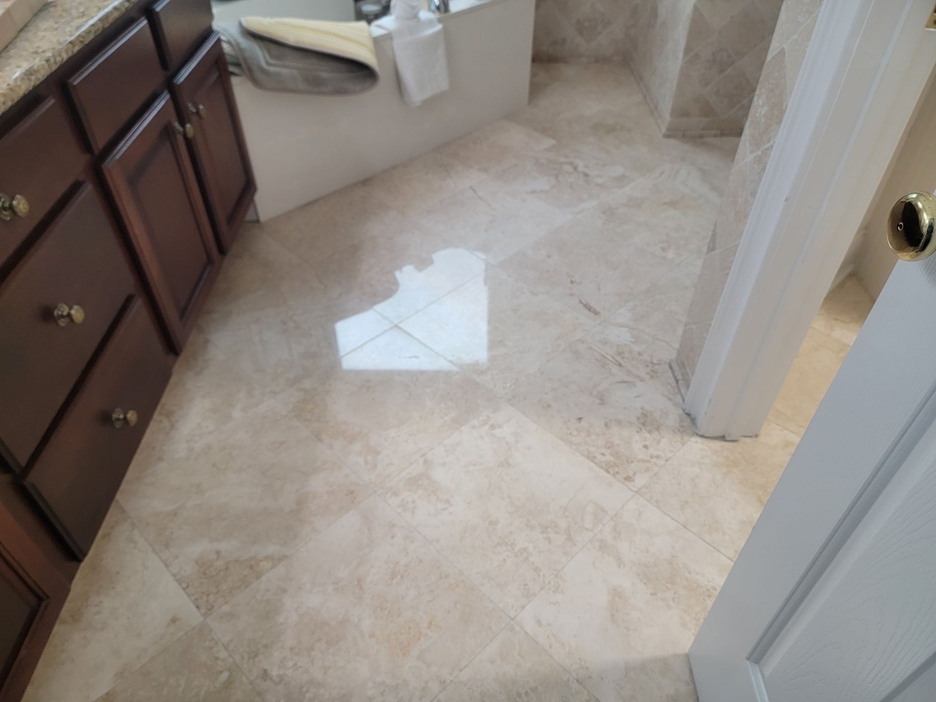 Bathroom with beige marble tile floor, dark wood cabinets, and white door.