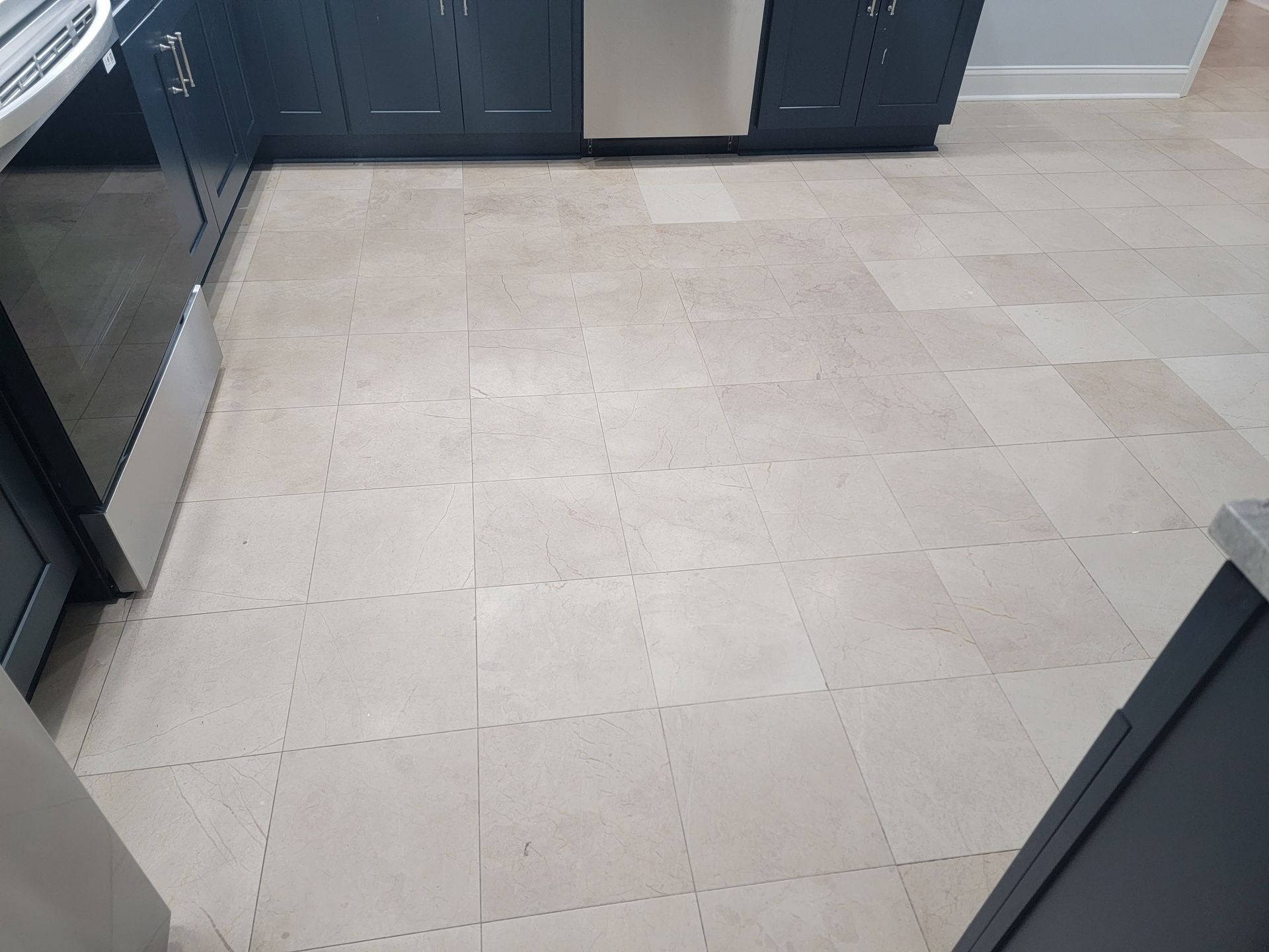 Beige tile flooring in a kitchen with dark blue cabinets and stainless steel appliances.